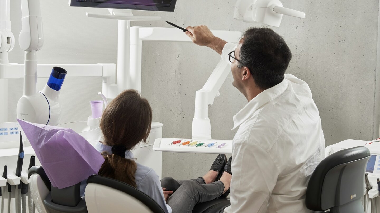 Chirurgien-dentiste présentant une radiographie dentaire à une patiente dans un cabinet lumineux